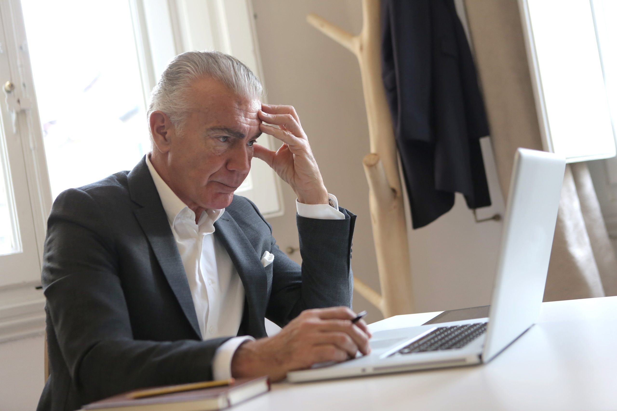 An elderly man contemplates what he sees on his laptop screen